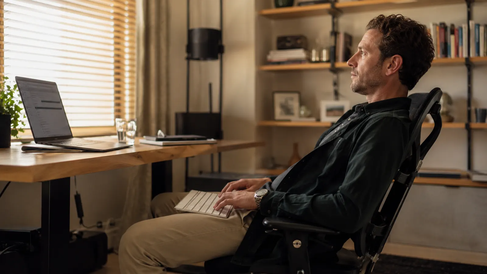 Remote worker leaning back comfortably at a home office desk using a wireless keyboard from a relaxed posture
